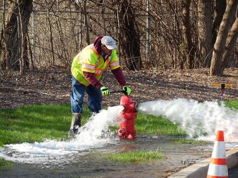 A City worker works on a fire hydrant that has water coming out of it.